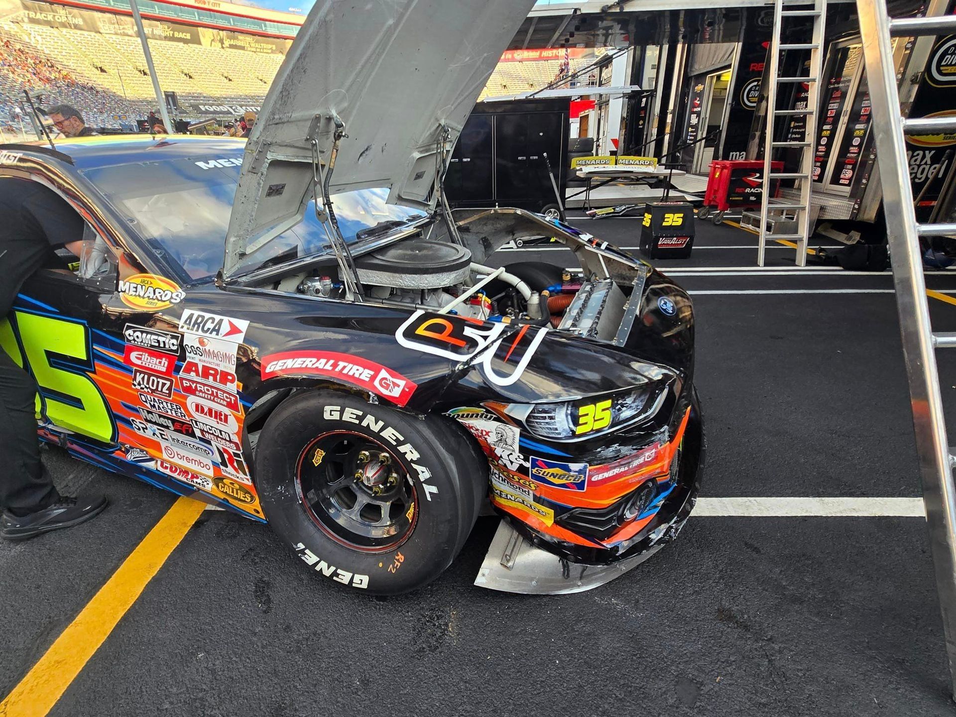 Black race car with hood open in pit lane, number 5 on the door, surrounded by equipment and crew area