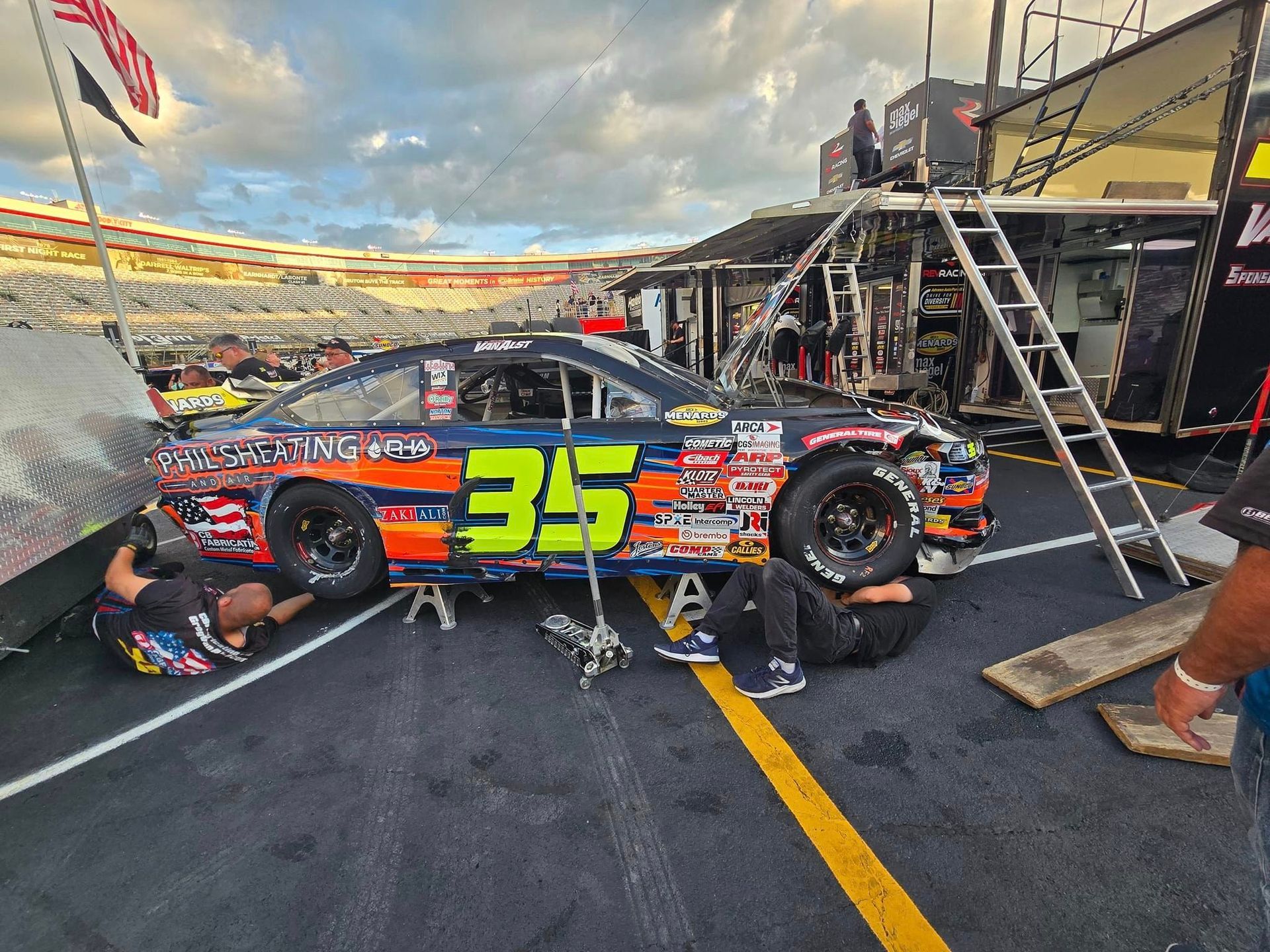 Race car #35 in colorful livery being serviced in a pit lane by crew members and equipment.