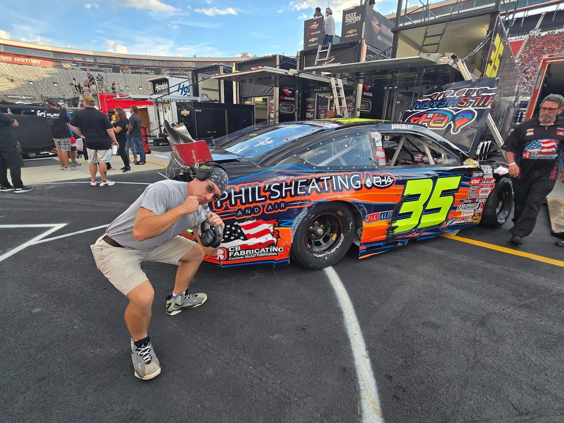 Race car in pit lane with crew working on black and orange #35 car at track