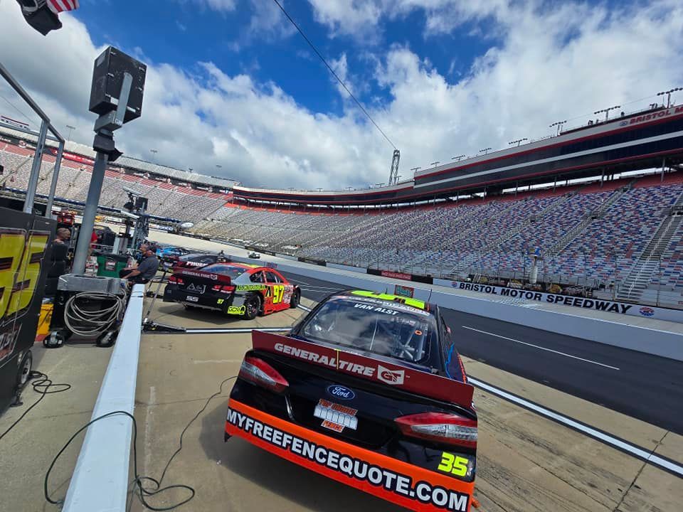 NASCAR race cars lined up in pit lane at a speedway under a bright blue sky