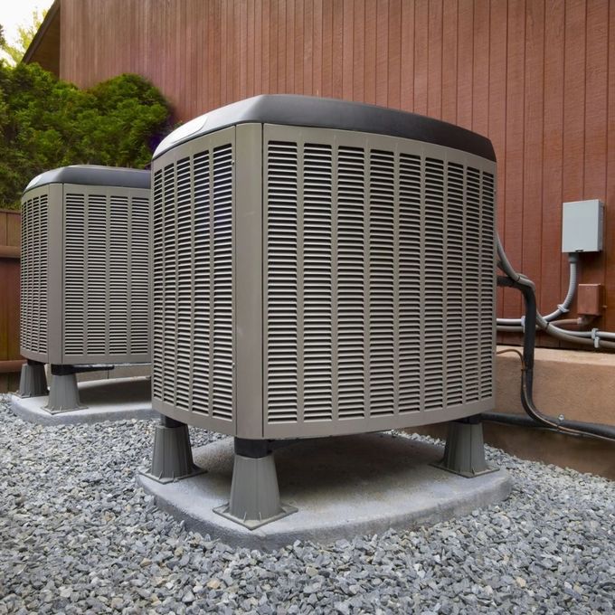 ACCA Website Two outdoor HVAC units on gravel beside a brown building wall