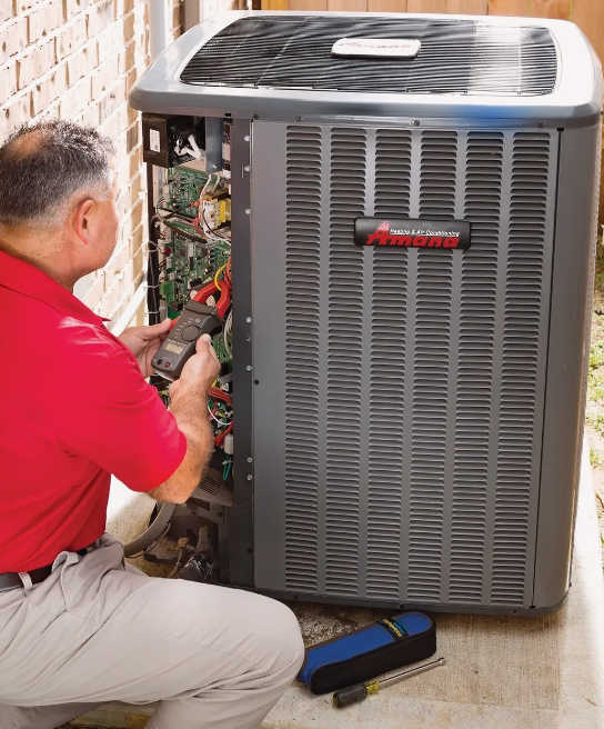 Learn more about Amana Heating and Air Conditioning Technician servicing a gray outdoor air conditioner with tools beside a brick wall