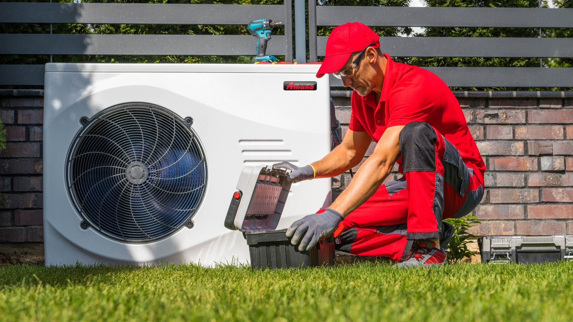 Technician in red uniform servicing an outdoor HVAC unit beside a house.