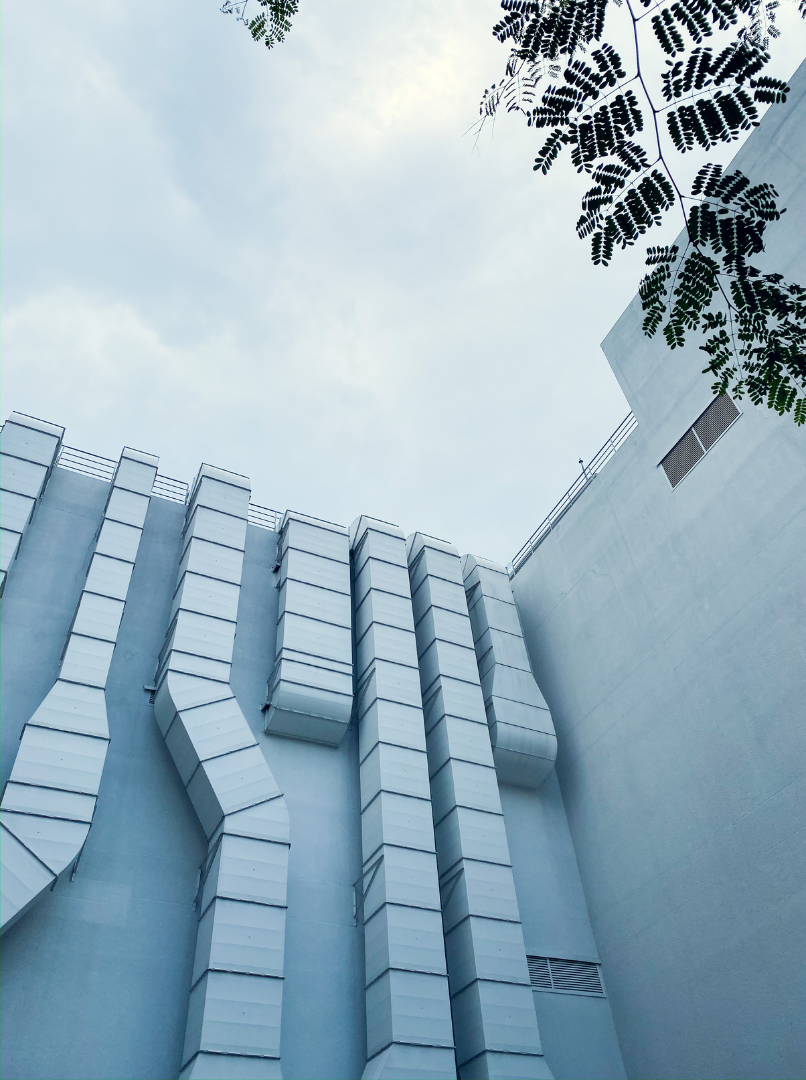 Contact Us Modern white building facade with geometric panels viewed from below against a cloudy sky