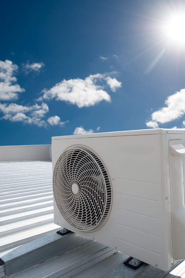 Contact Us! Outdoor air conditioner unit on a rooftop under a bright blue sky with clouds.