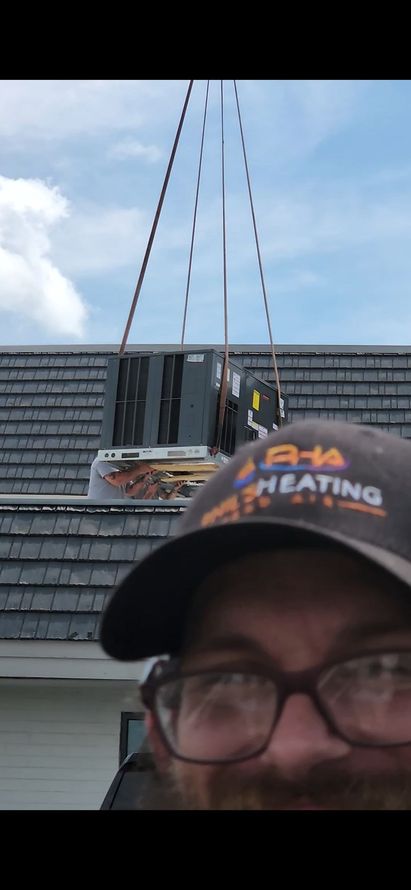Person in black cap and glasses in foreground, rooftop HVAC unit being lifted by crane behind them.