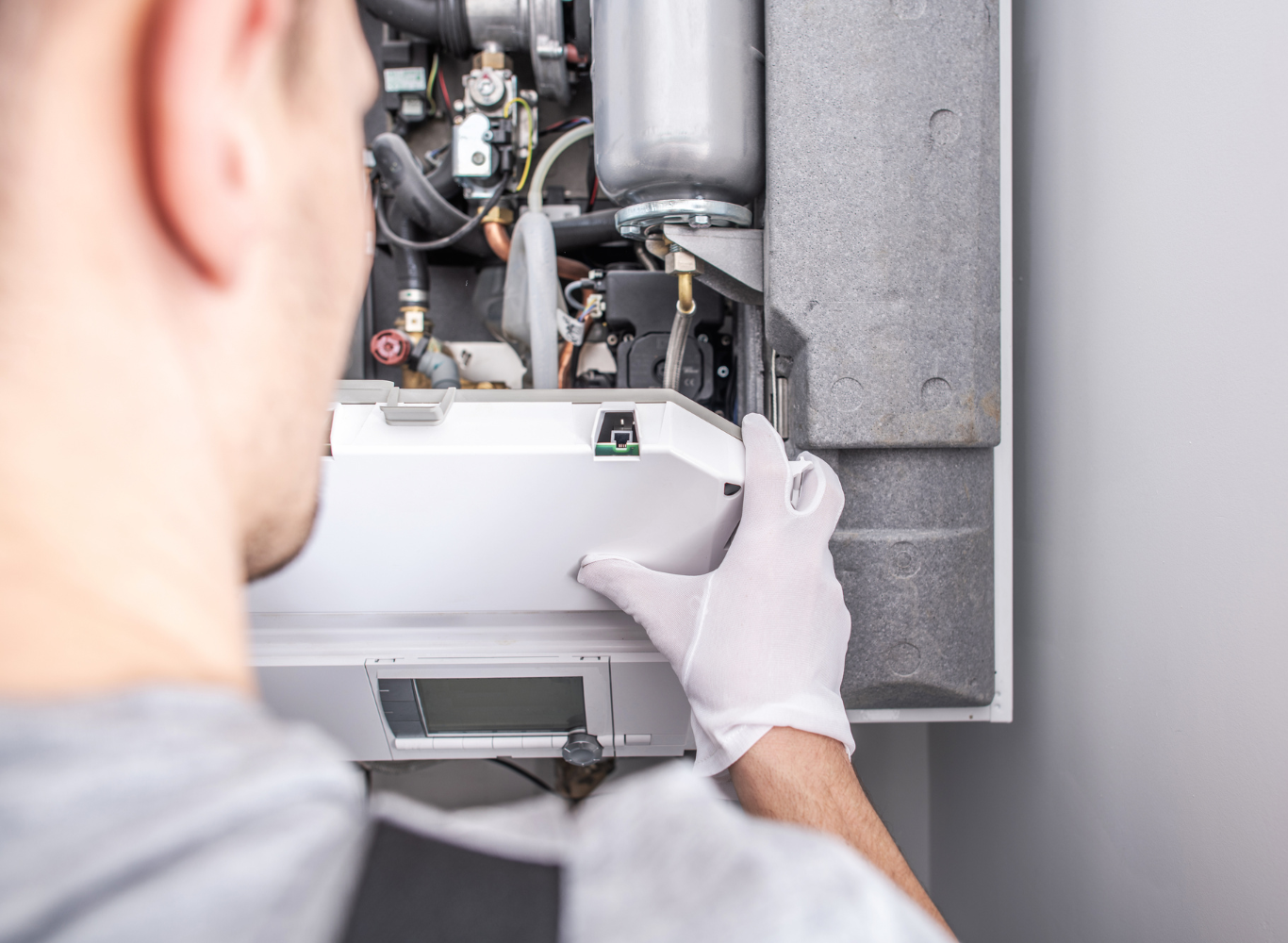 Technician in white gloves inspecting an open wall-mounted HVAC or boiler unit with tools inside.