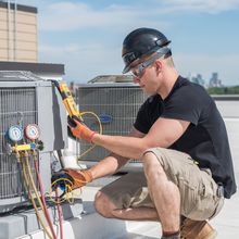 Technician inspecting HVAC unit with gauges and tools on a rooftop