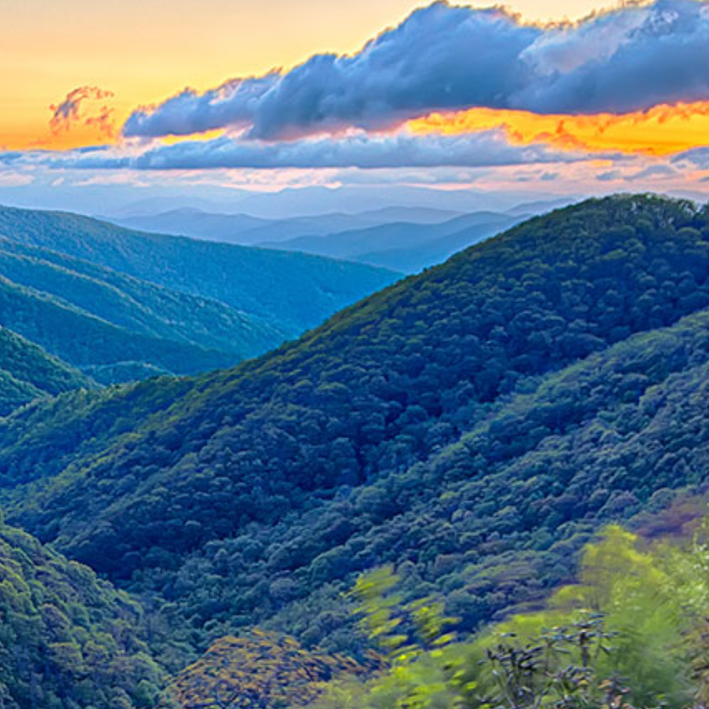 Blue-green mountain ridges under a dramatic orange sunset sky with layered clouds