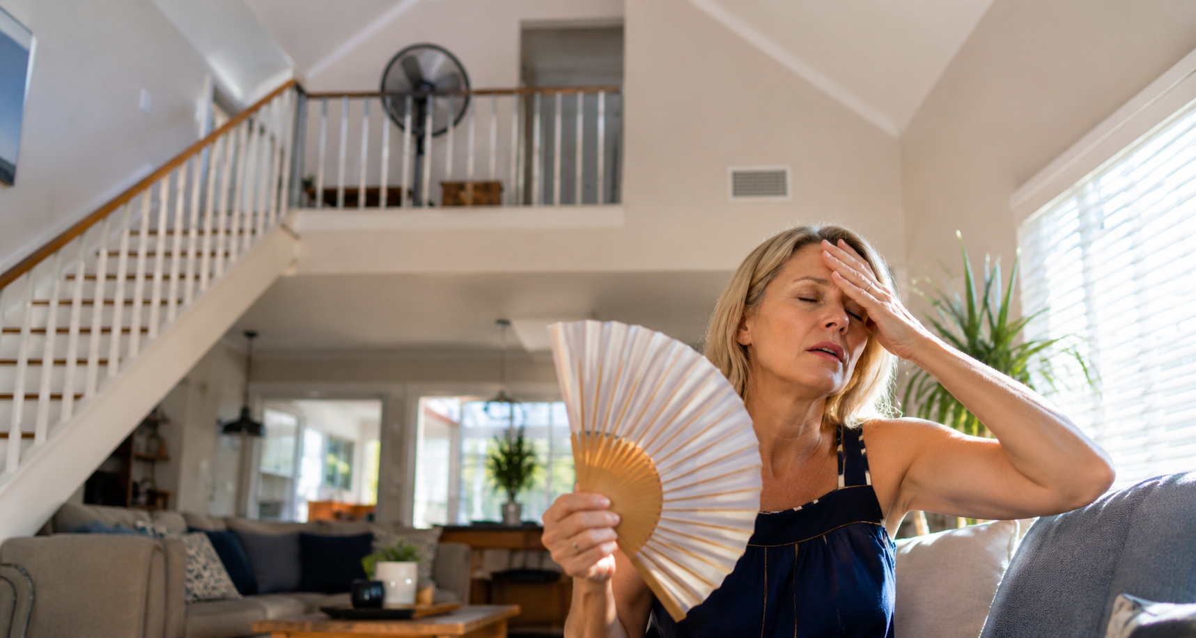 Woman fanning herself on a bright sofa in a sunlit living room
