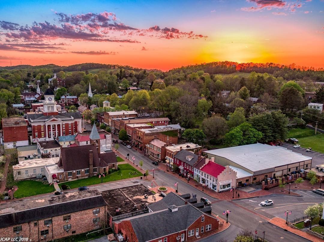 Aerial view of a small town at sunset with red-roofed buildings, trees, and a colorful sky.