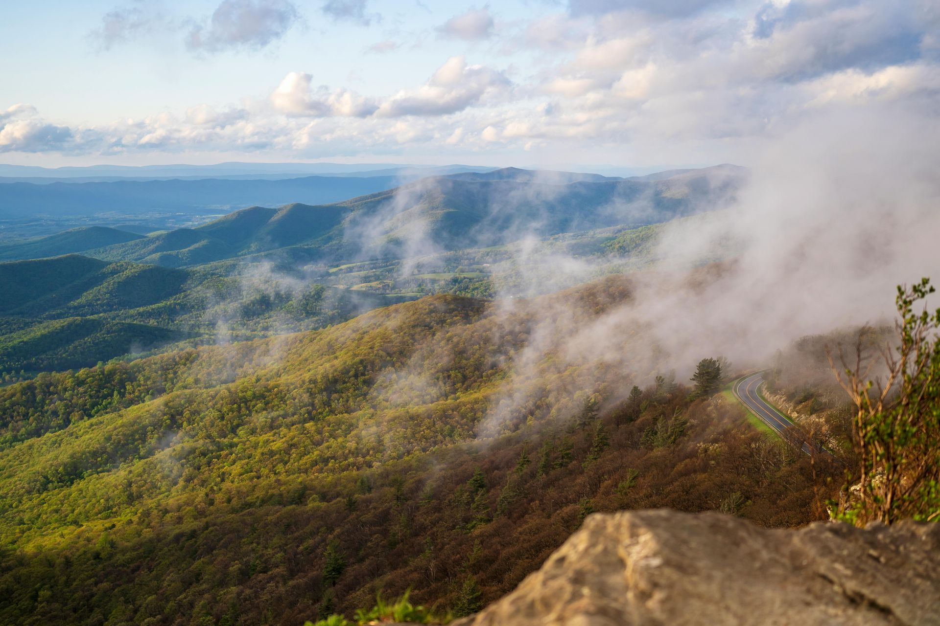 A view of a mountain covered in fog and clouds from a cliff.