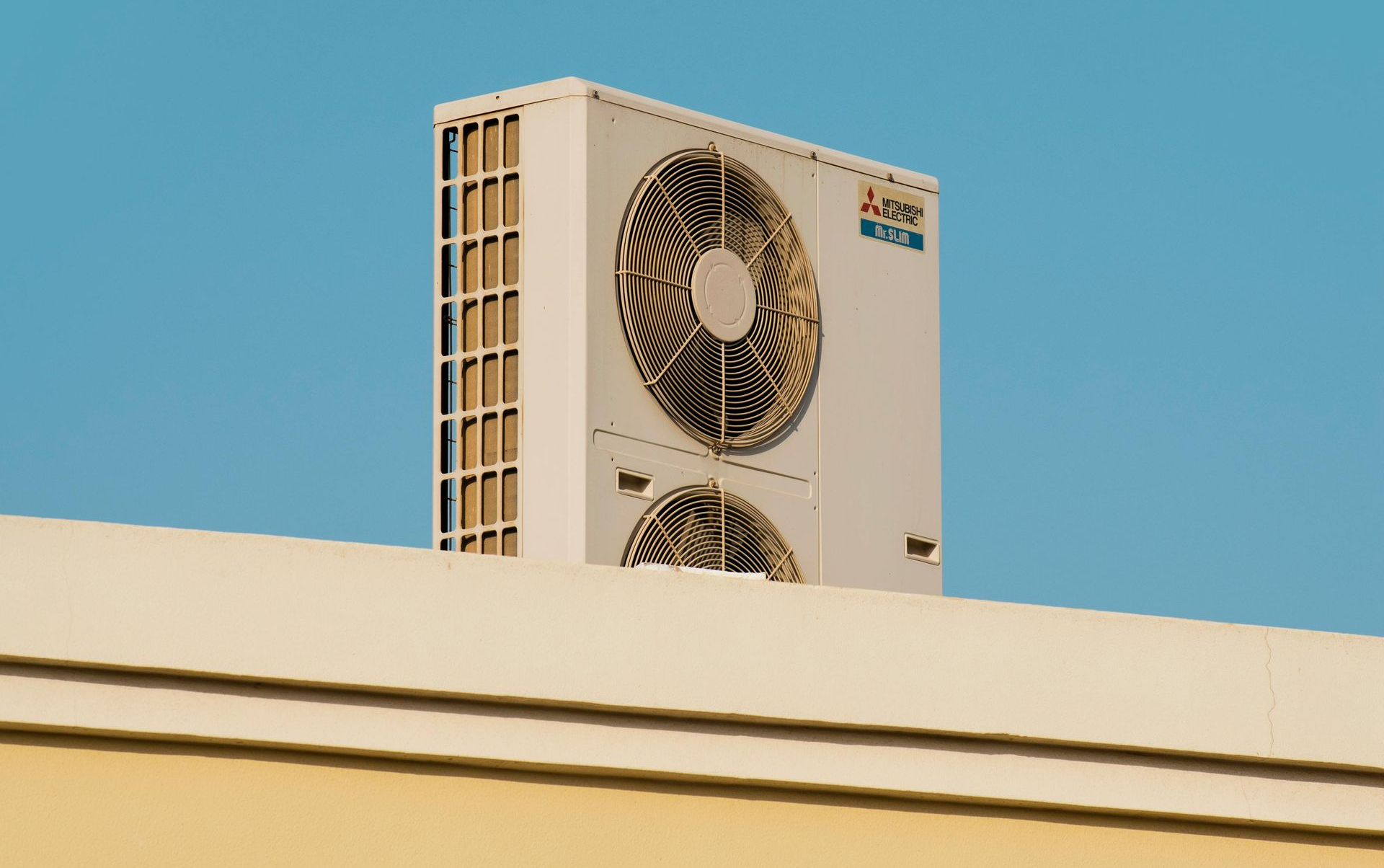 Our Services Rooftop air-conditioning unit above a beige building against a clear blue sky