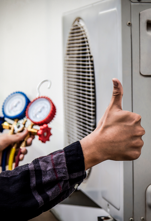 Our Services Technician giving a thumbs-up beside an air conditioner, with blue and red gauges attached.