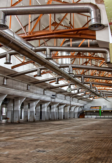 Industrial HVAC Services Empty industrial interior with exposed metal ducts, steel beams, and a dirt floor.