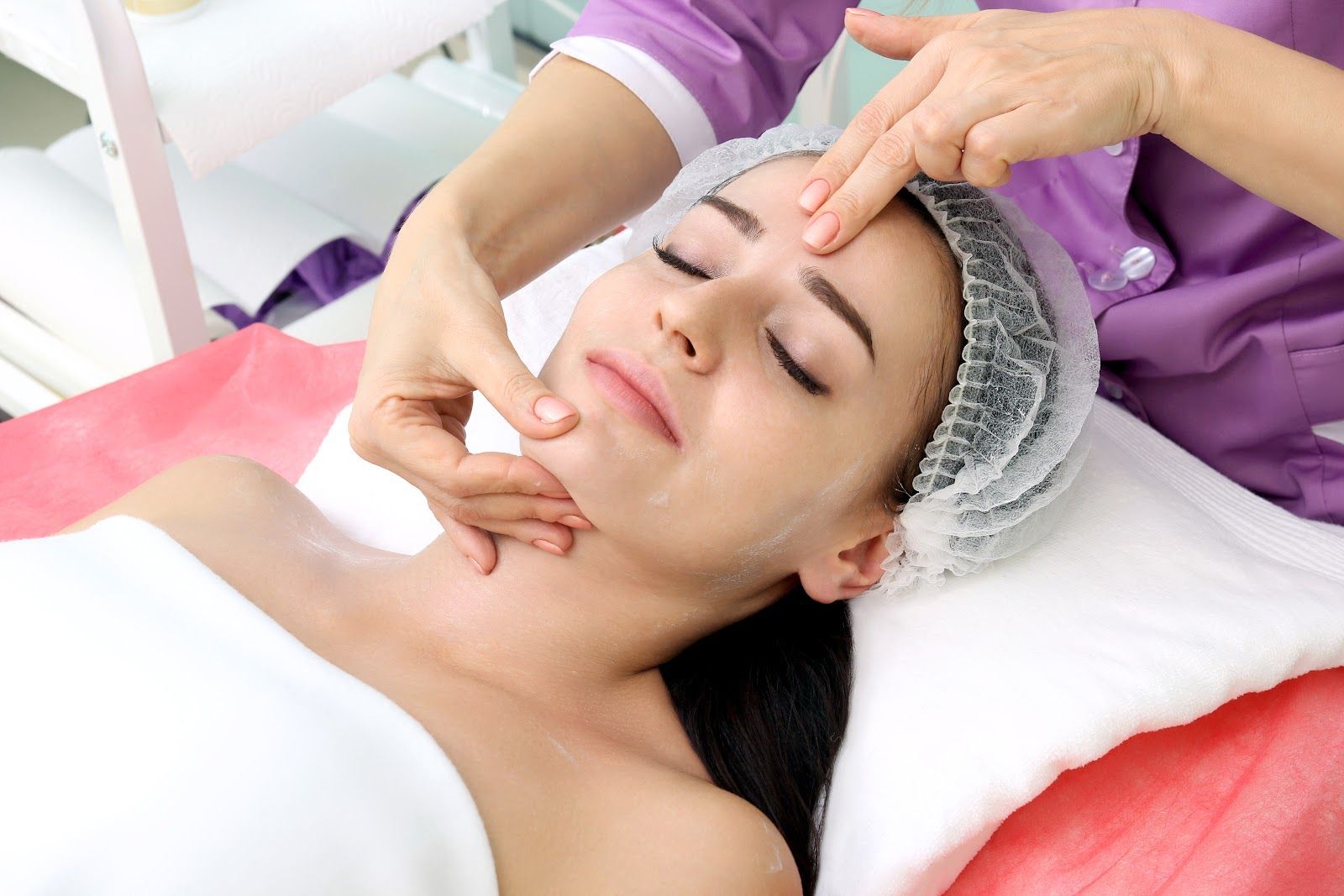 Facial massage at a spa, with a woman lying on a treatment bed wearing a towel headband