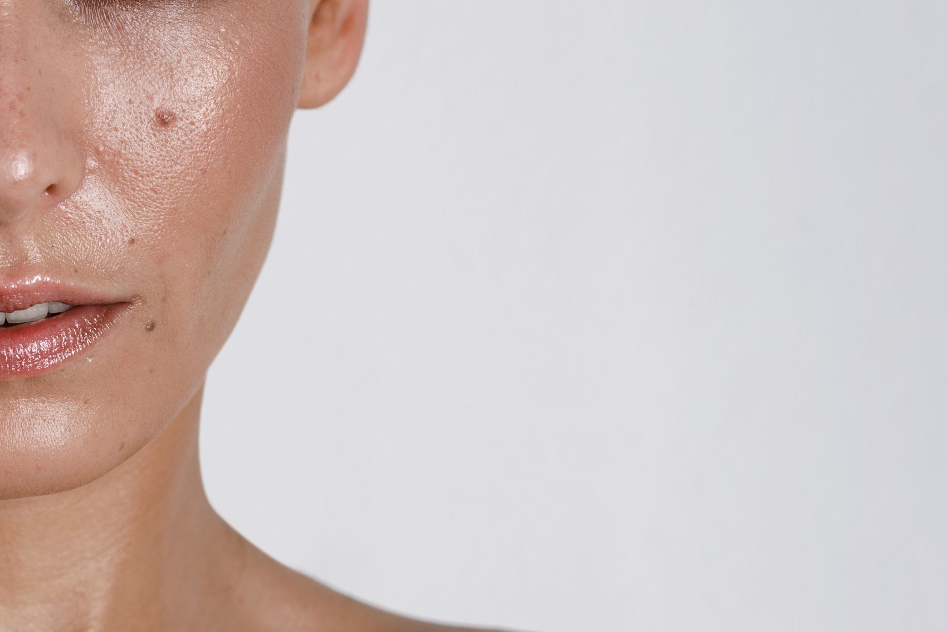Close-up of a dewy face with glossy lips and clean skin against a white background