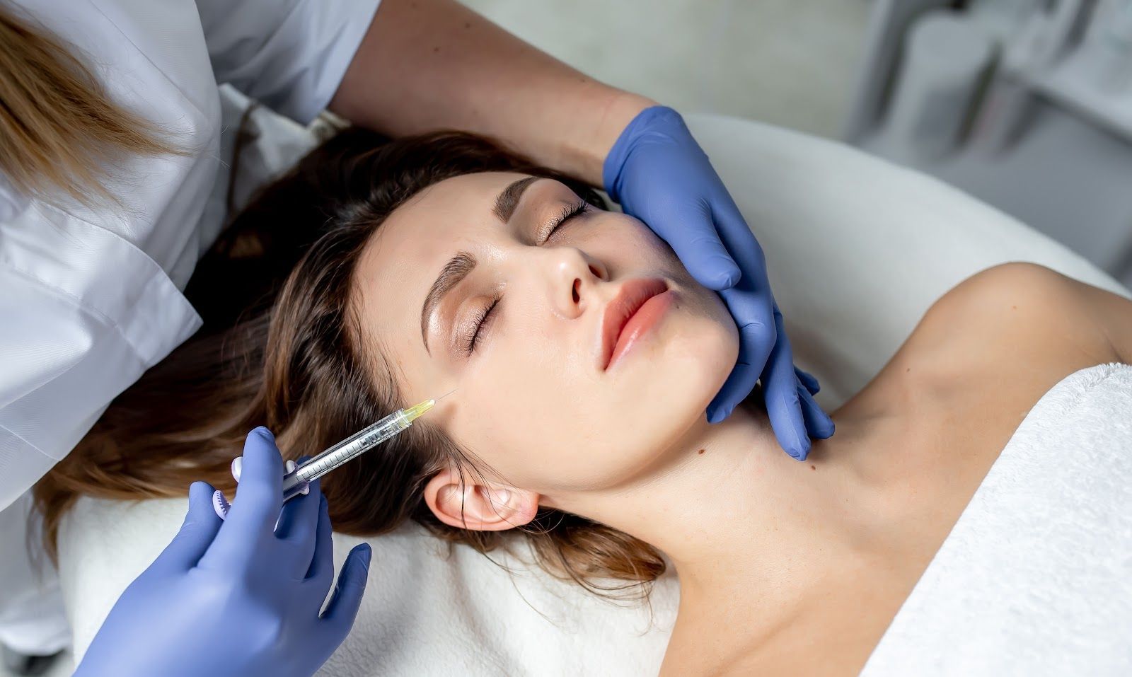 Gloved clinician injecting a woman’s cheek during a cosmetic facial procedure
