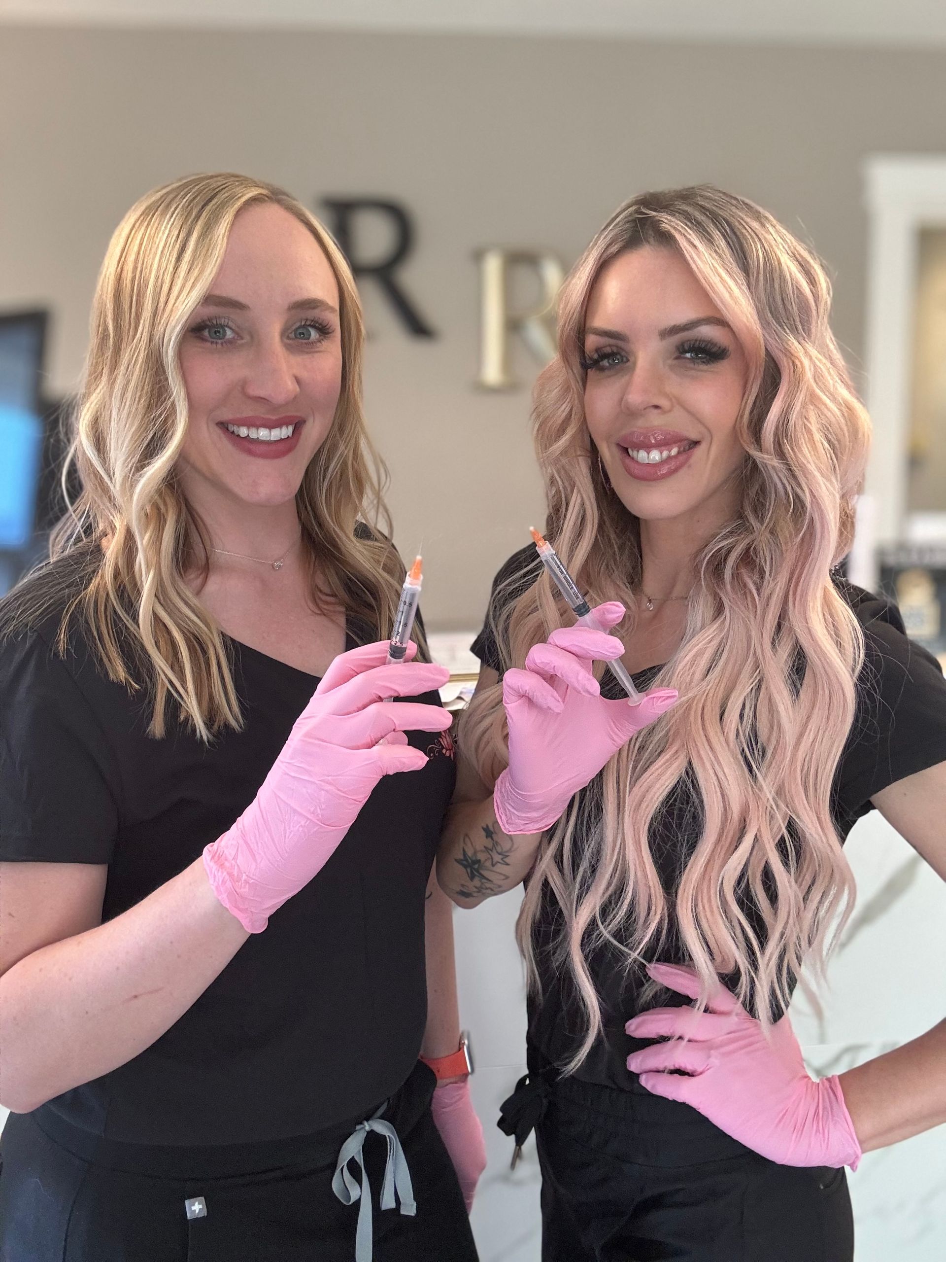 Two women wearing pink gloves are holding syringes in their hands.