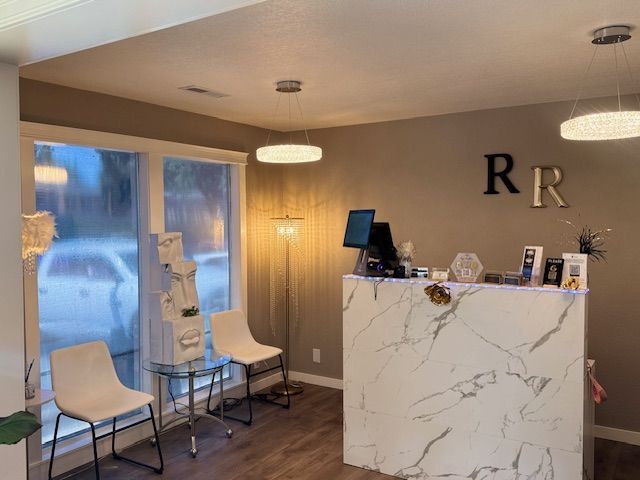 Small reception area with white chairs, marble-front desk, wall lights, and an “RR” sign.