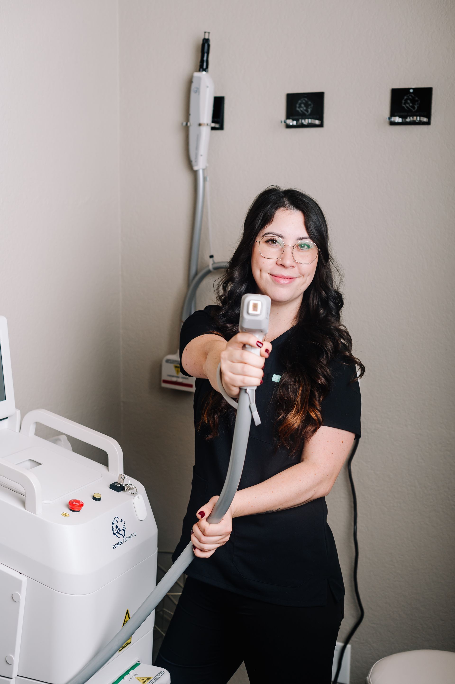 A woman is standing in front of a machine holding a wand.
