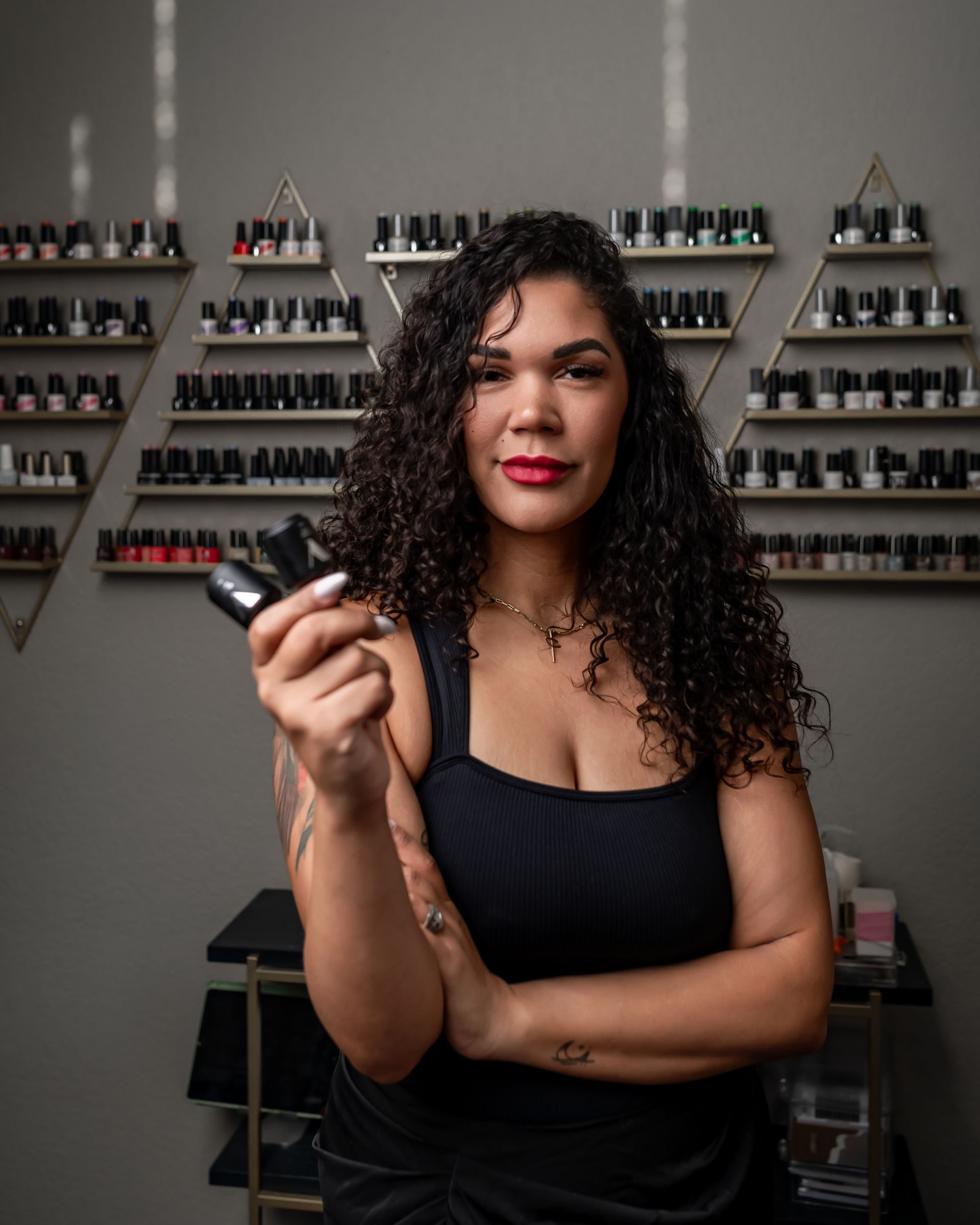 A woman is standing in front of a wall of nail polish shelves holding a bottle of nail polish.