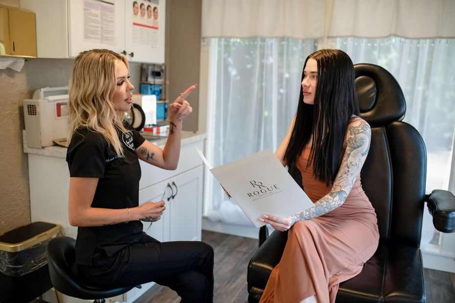 Two women in a consultation, one gesturing while the other holds papers in a medical office