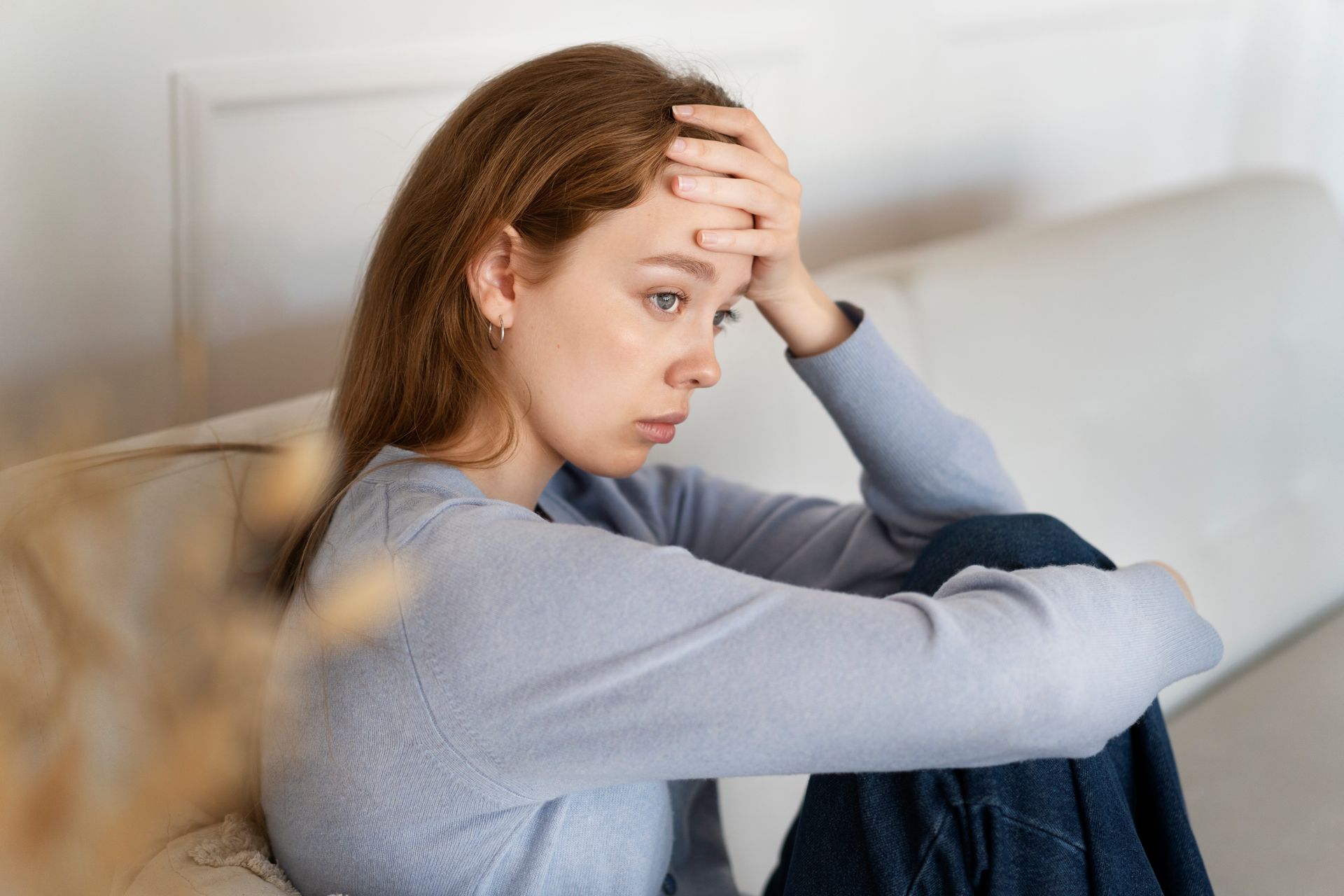 A woman is sitting on a couch with her head in her hands.