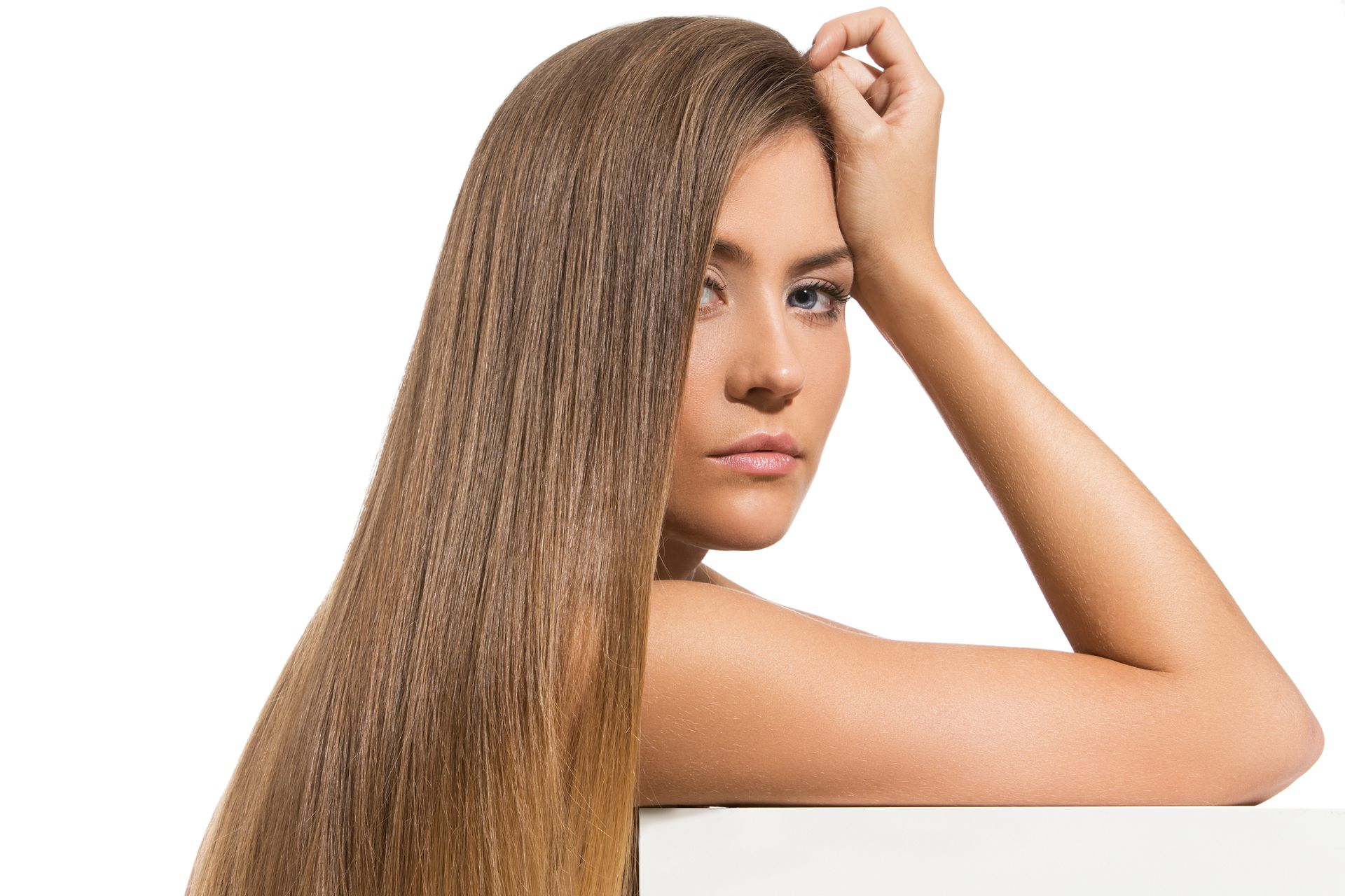 A woman with long hair is leaning against a white wall.