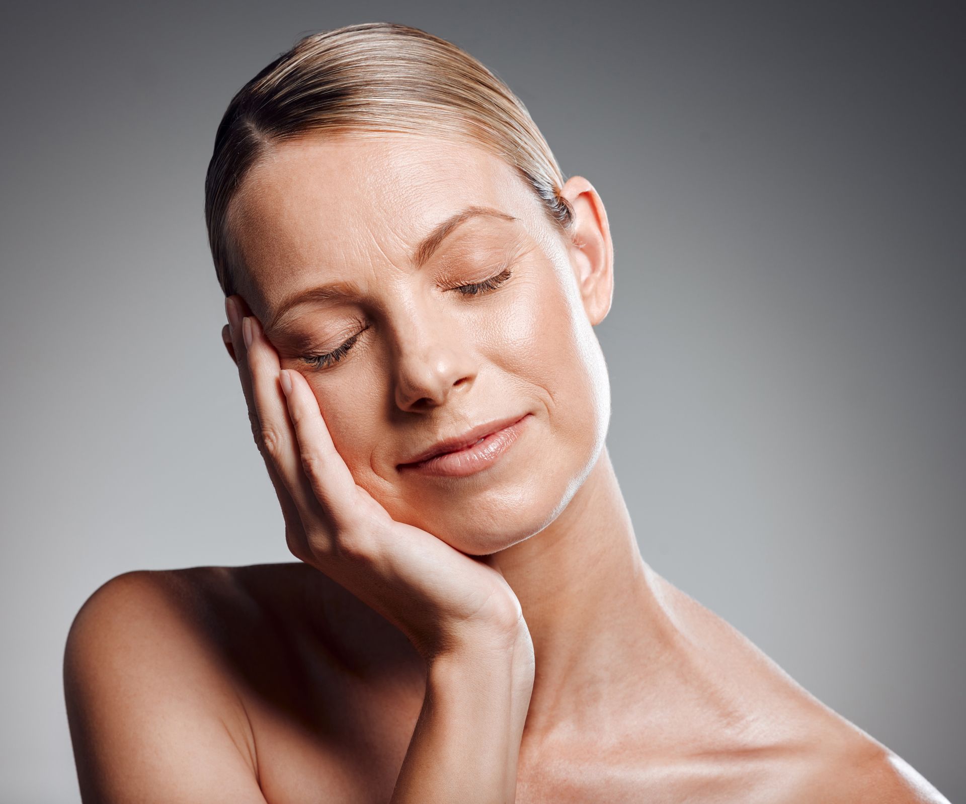 A woman with her eyes closed is touching her face with her hand.