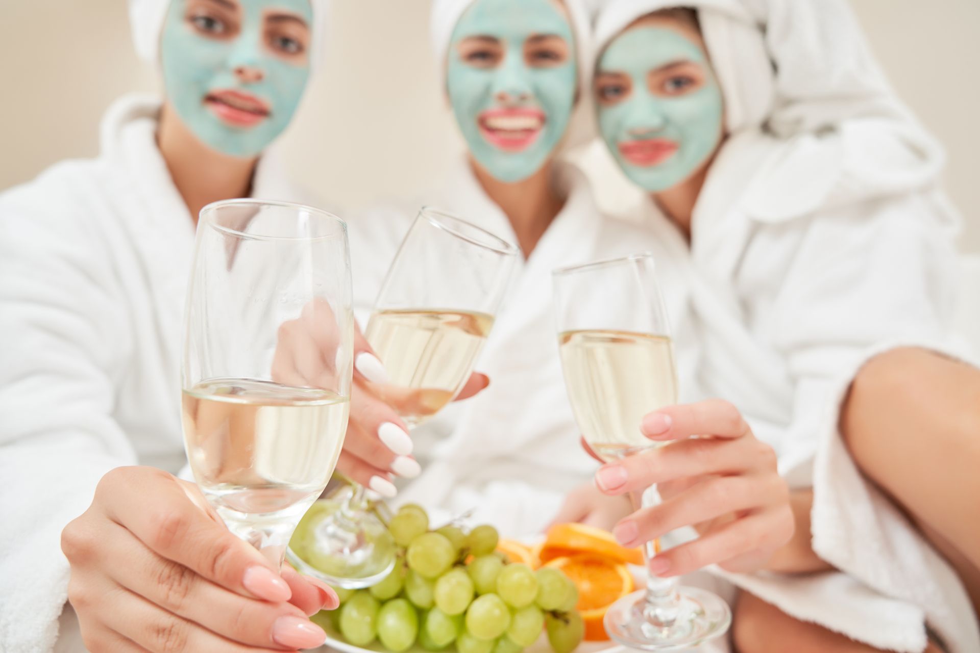 Three women with face masks are toasting with champagne and grapes.