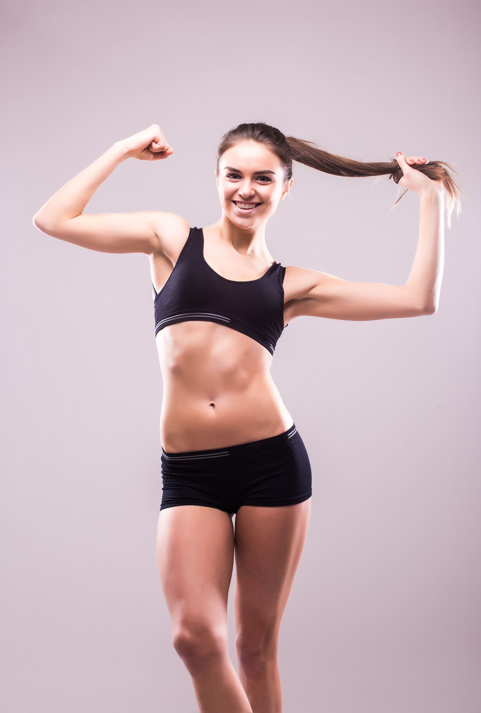 A woman in a black sports bra and shorts is flexing her muscles.