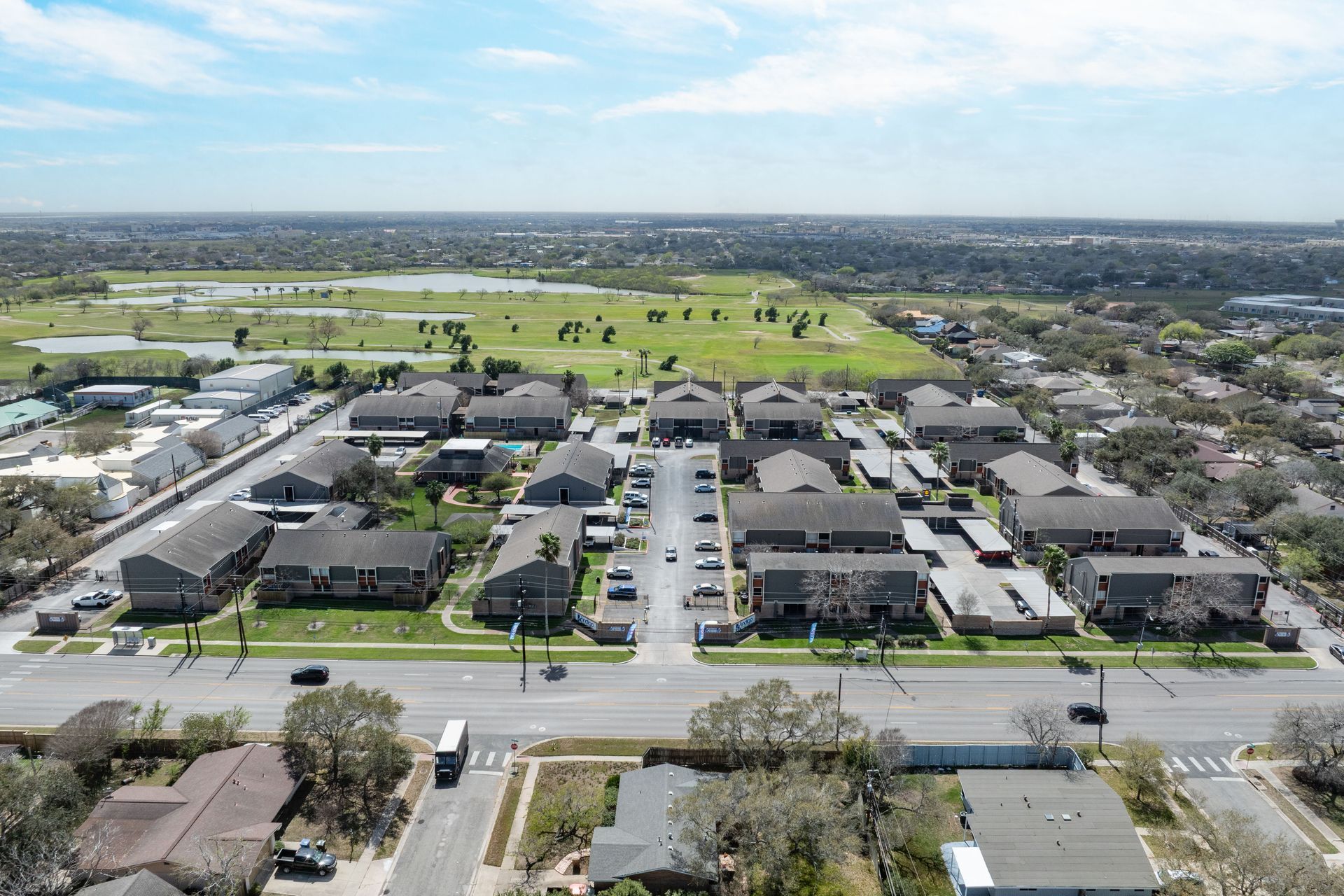 Aerial view of a suburban neighborhood with rows of houses, streets, and open green fields in the distance