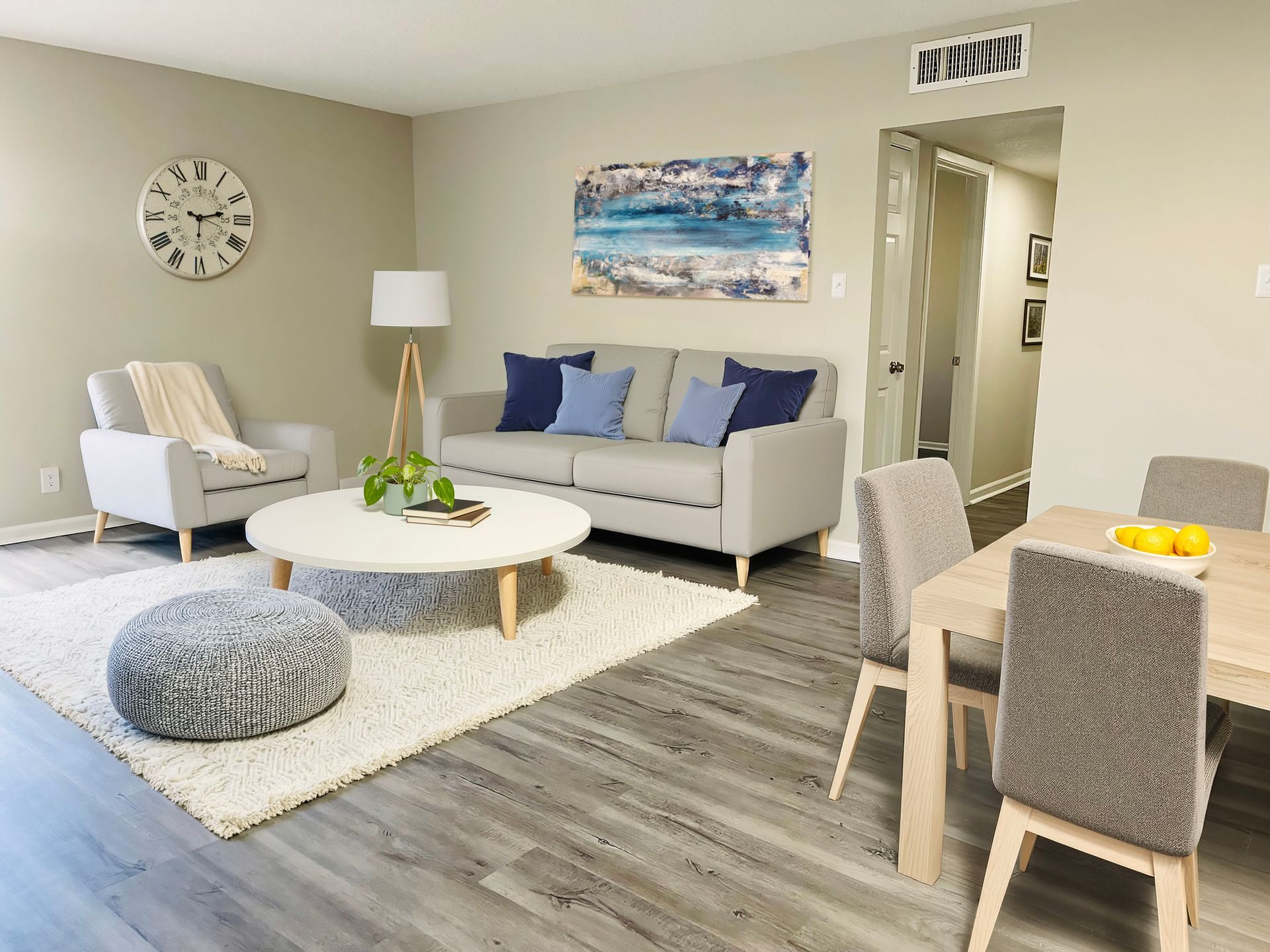 Bright living room with gray sofa, white rug, round coffee table, armchair, and dining nook by a doorway
