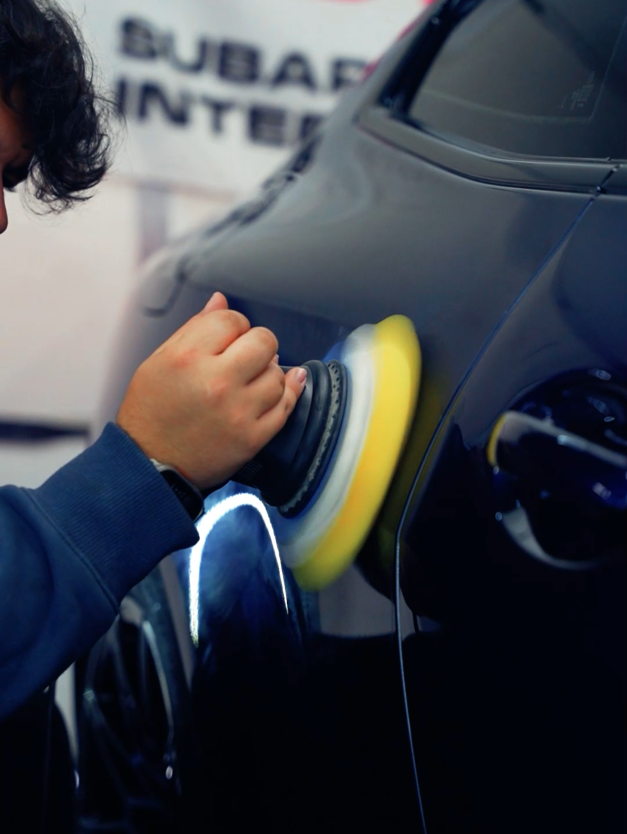 Person wearing black gloves wiping a black car door handle with a blue cloth.