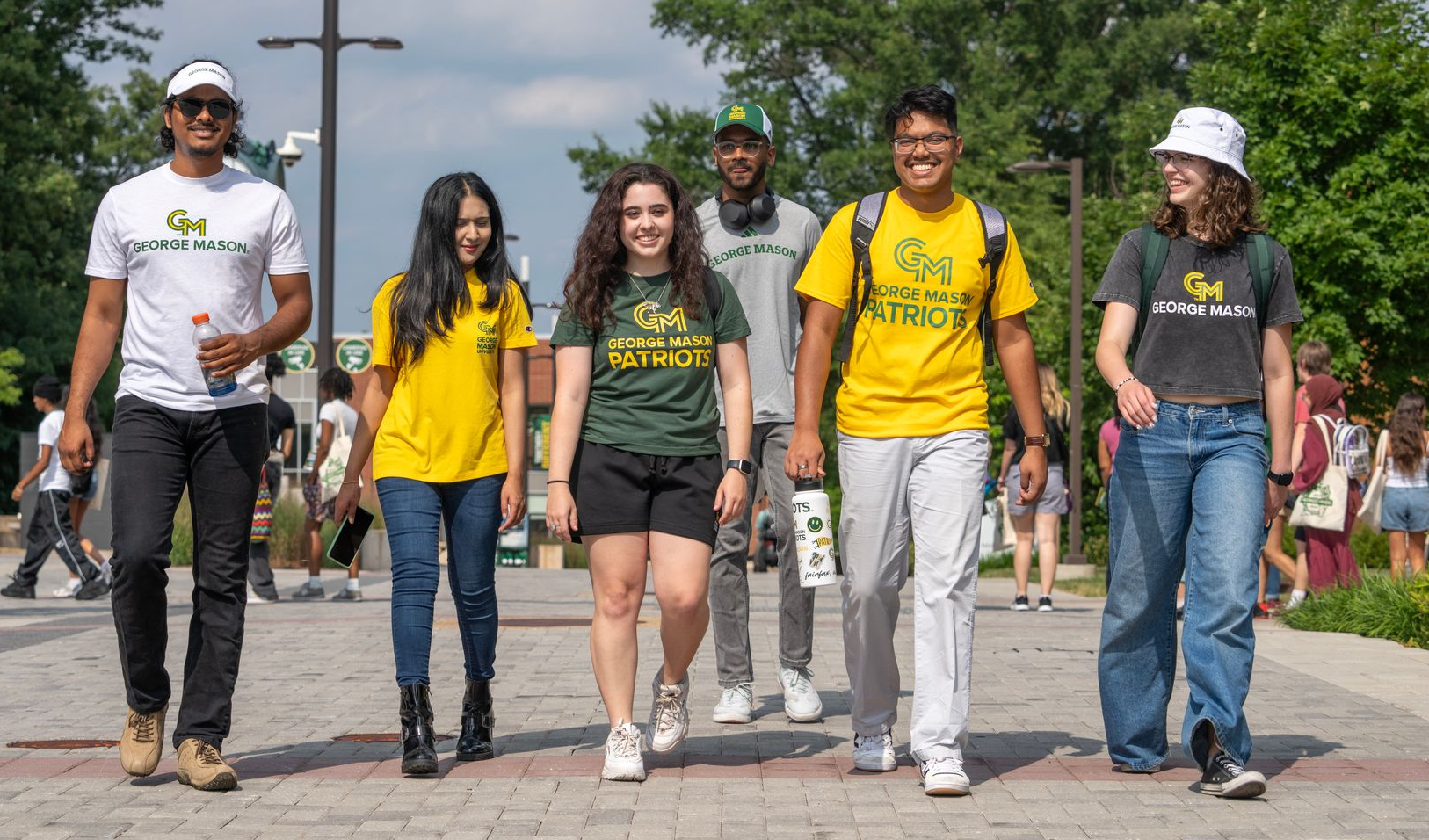 Group of people walking outdoors on a sunny day, several wearing bright yellow shirts and jeans.