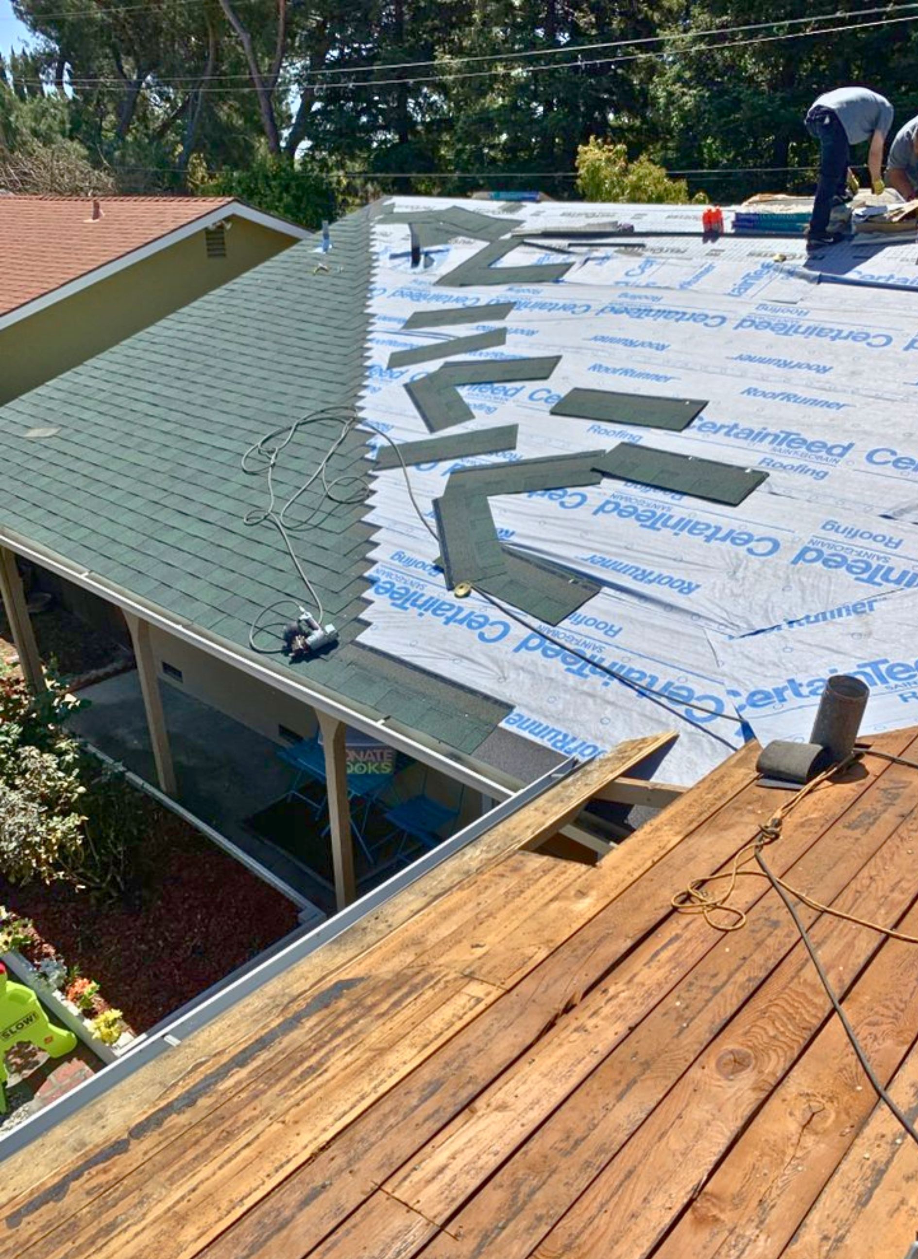 A man is laying shingles on the roof of a house.