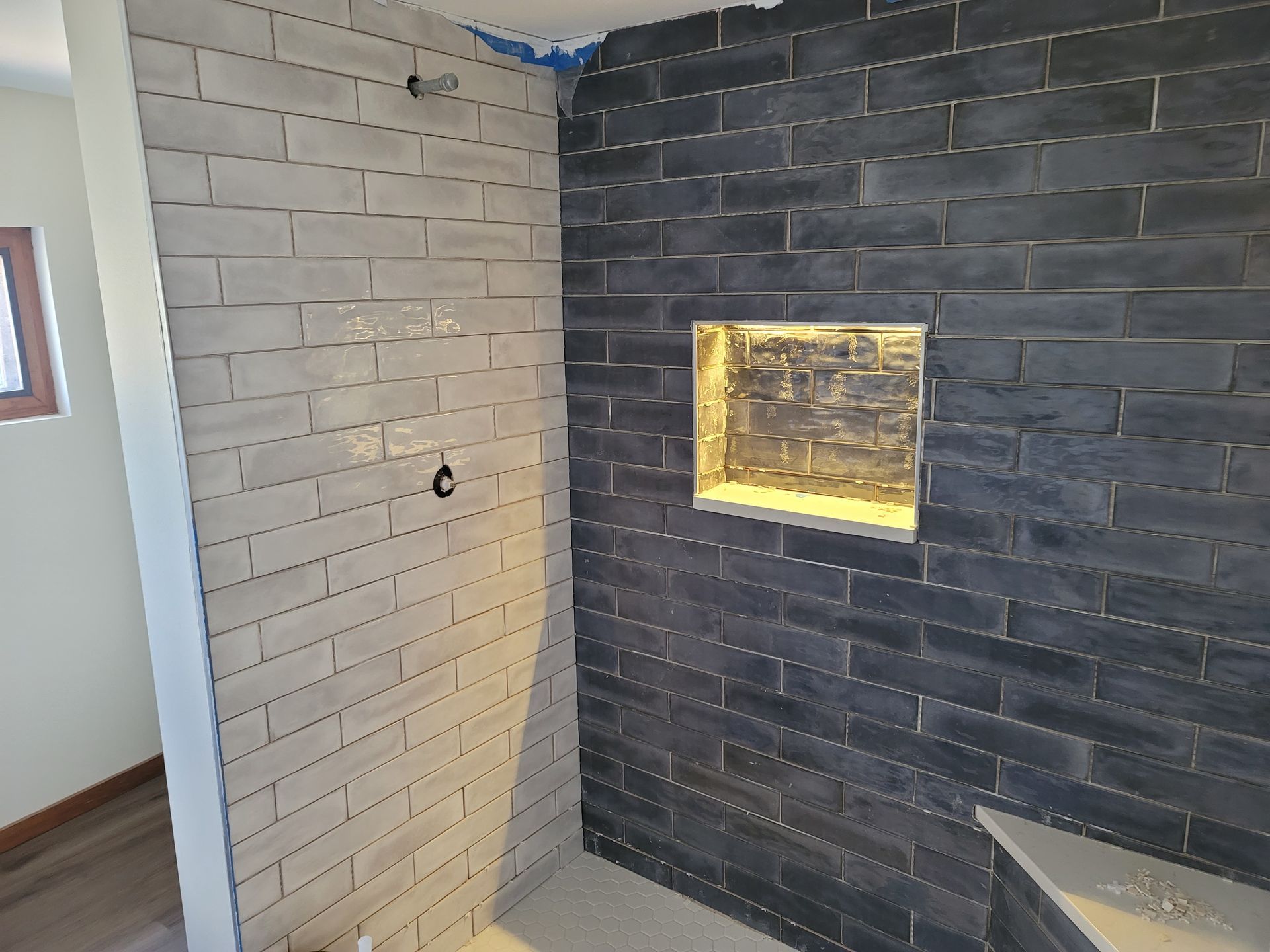 A shower under construction with a light grey brick wall on the left and a dark charcoal brick wall with a recessed niche.