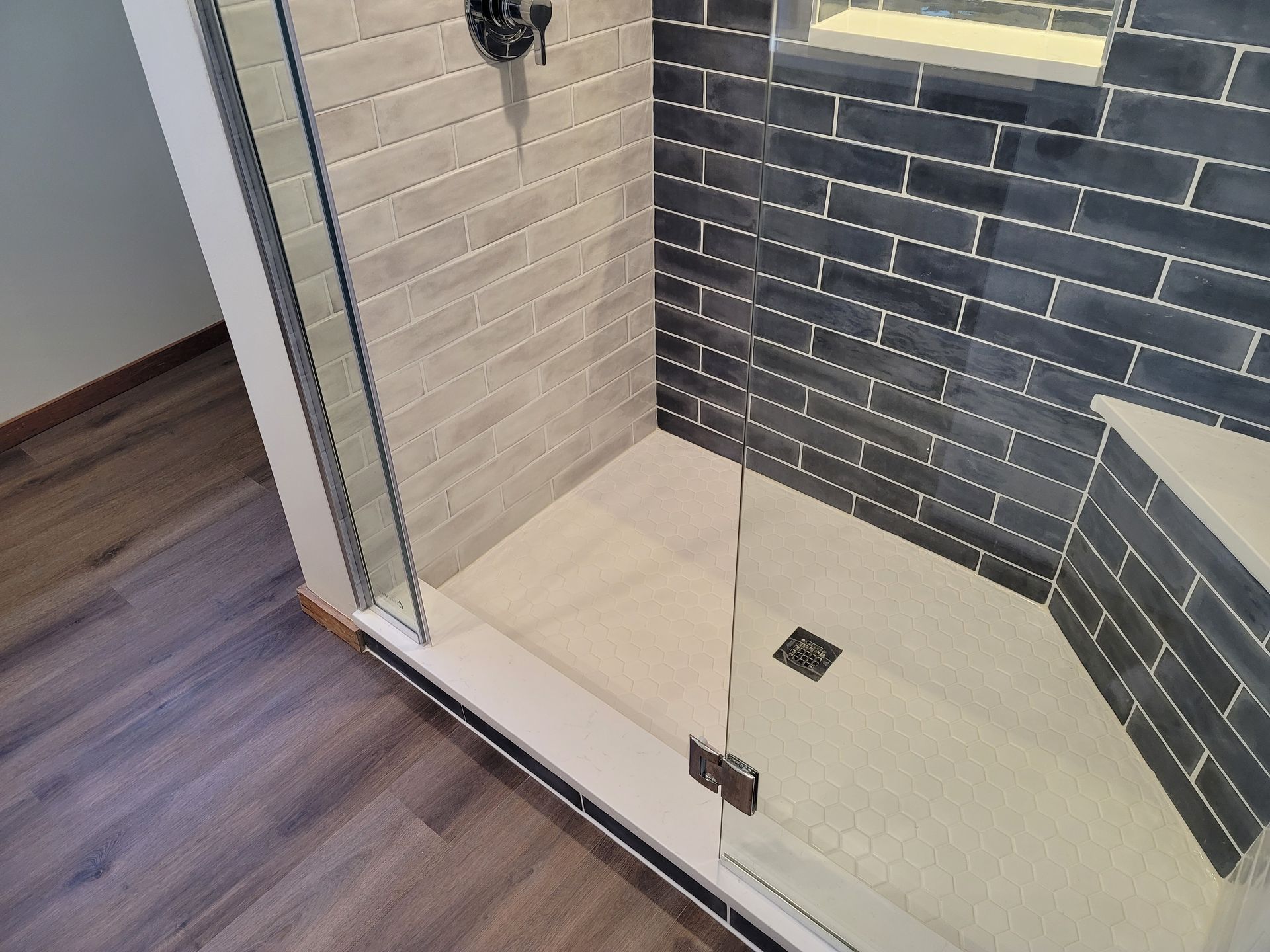 Bathroom with white shower and toilet, wood-look floor tiles, white vanity, and light blue walls.