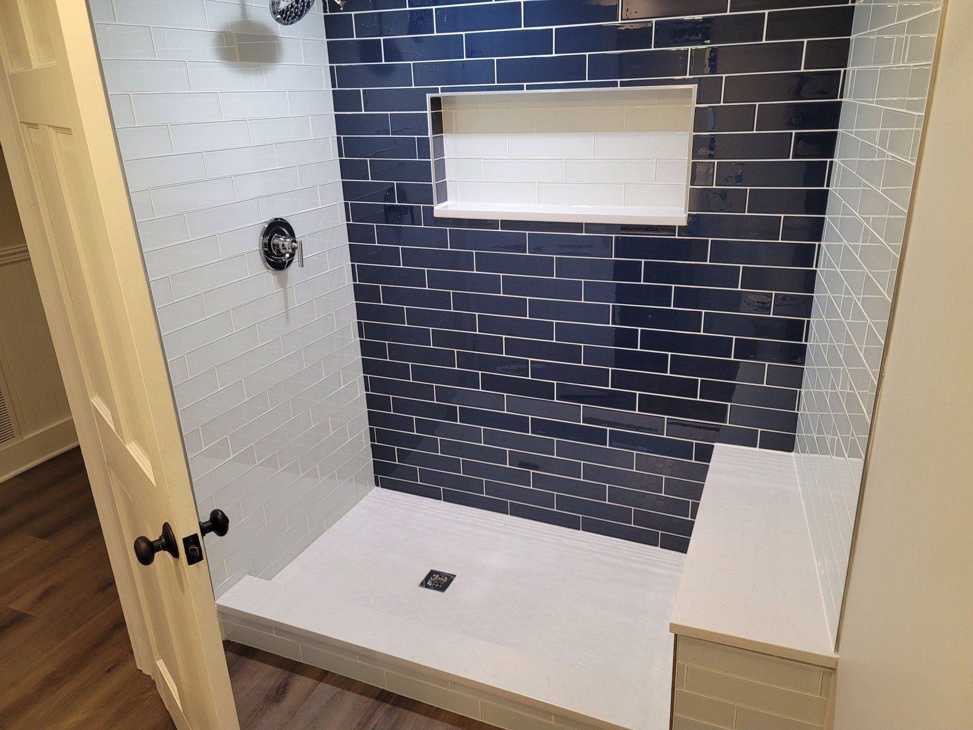 Shower with square rain shower head, hand shower, and brushed metal fixtures against marble-like tile walls.