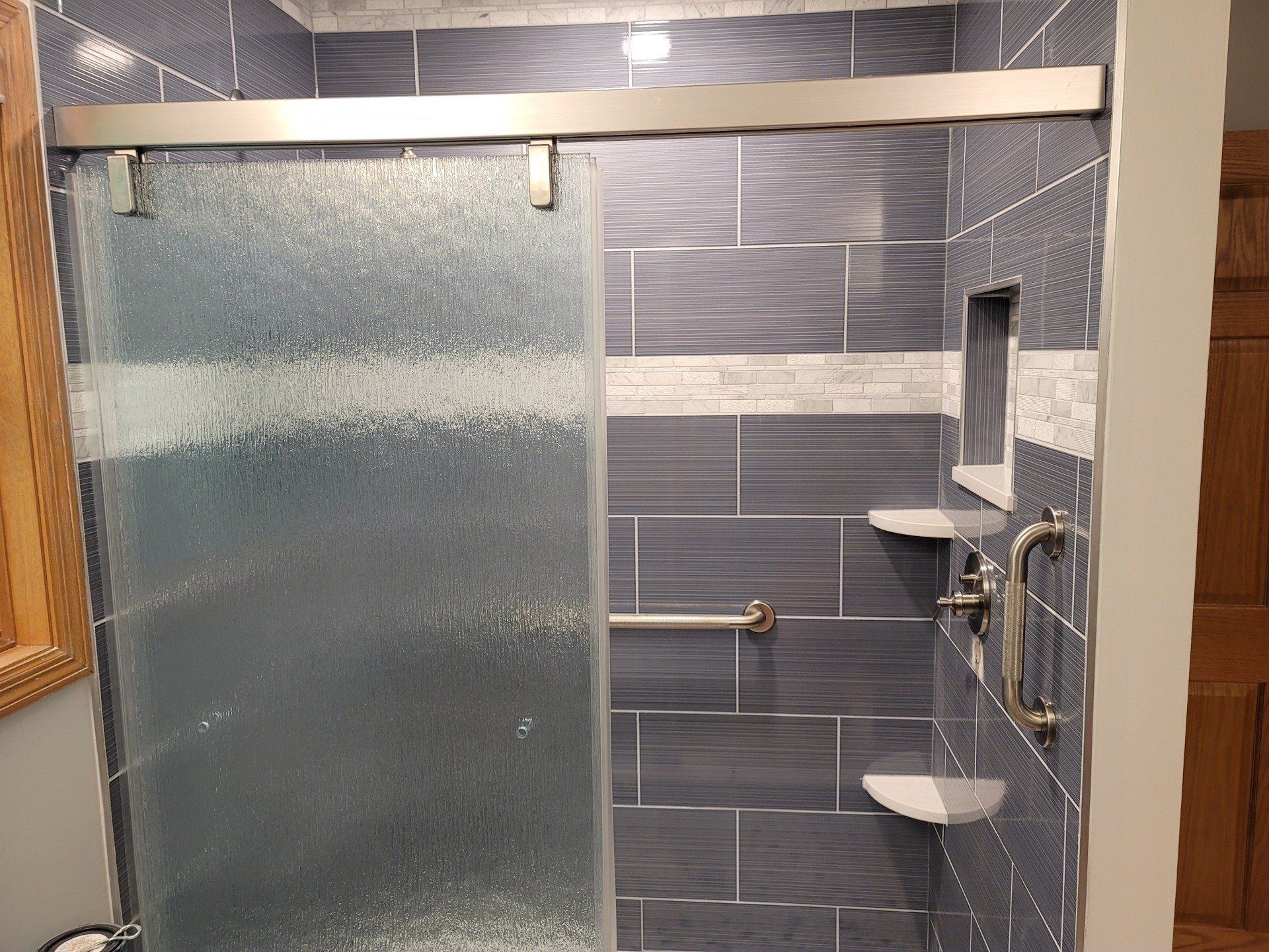 Bathroom with copper bathtub against a stone wall, glass shower, wooden vanity, and tiled floor.