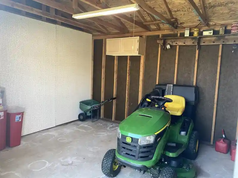 A green john deere lawn mower is parked in a garage.