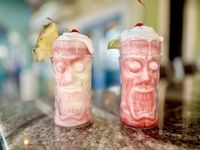 Two pink tropical tiki drinks with pineapple garnish on a bar counter
