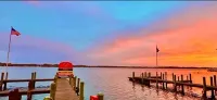 Sunset over a calm lake with wooden docks and red-lit boats, reflected in pink-orange sky