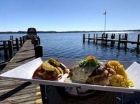 Plated seafood meal on a dockside table overlooking calm water and a wooden pier under a clear sky
