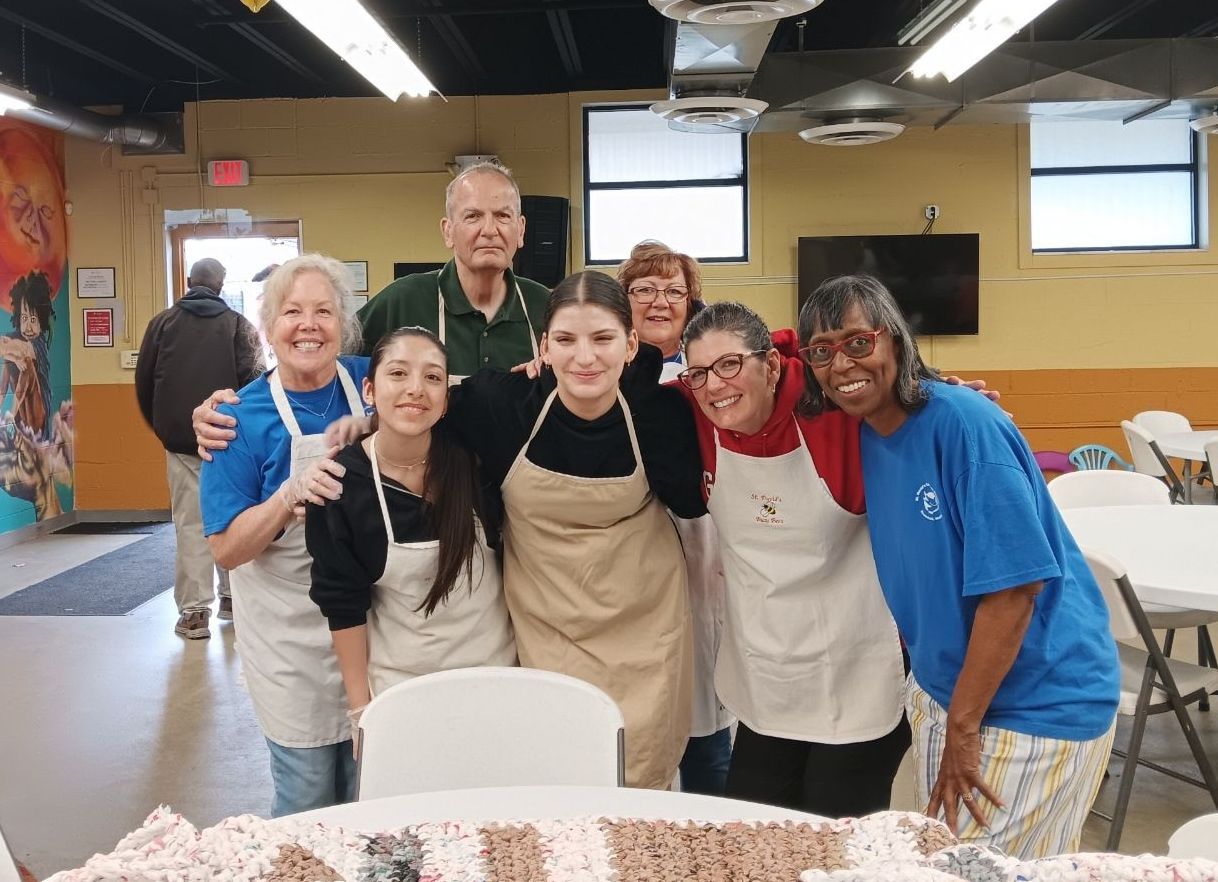 Group of 7 volunteers wearing aprons, at soup pantry.