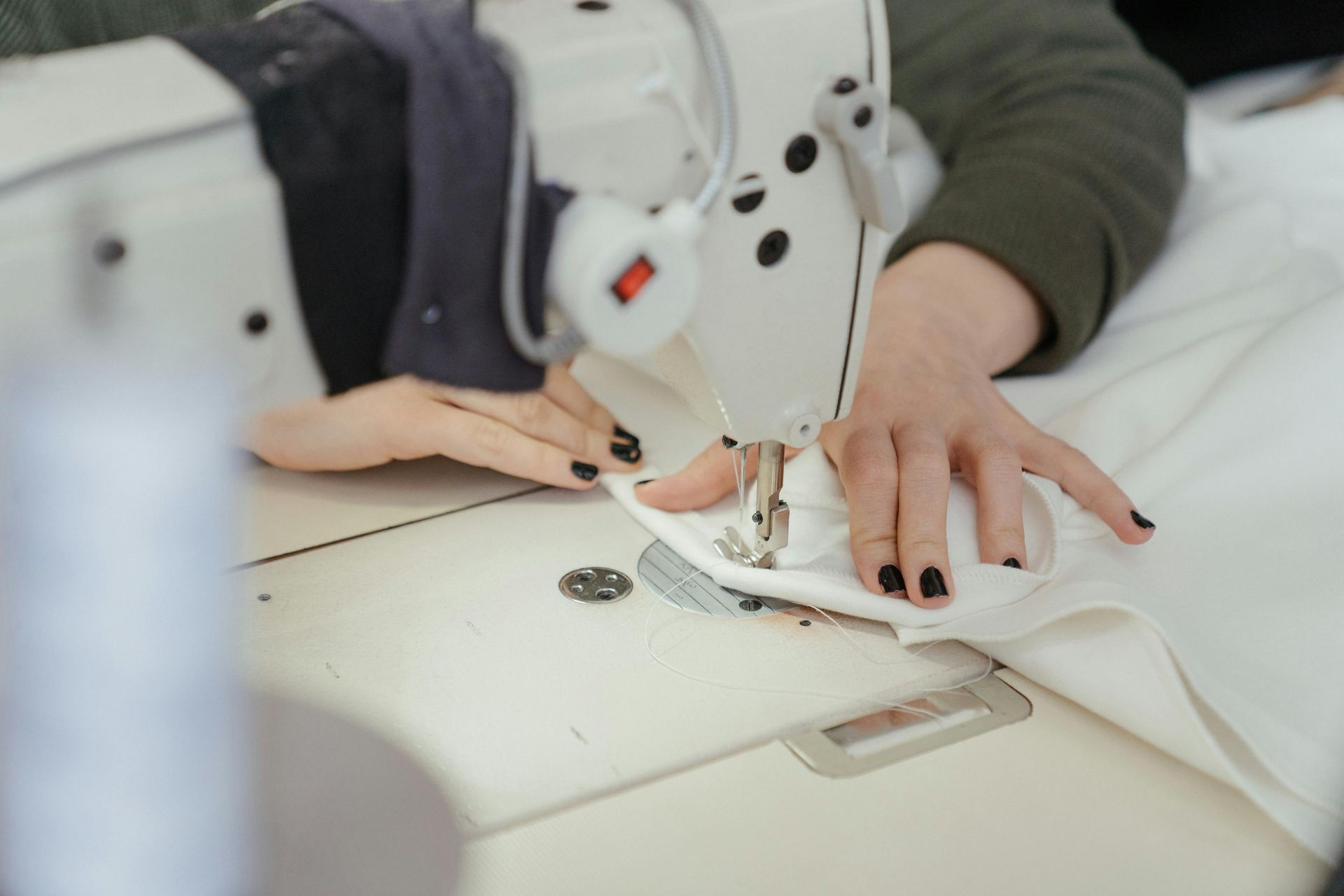 hands at a sewing machine, sewing white fabric.