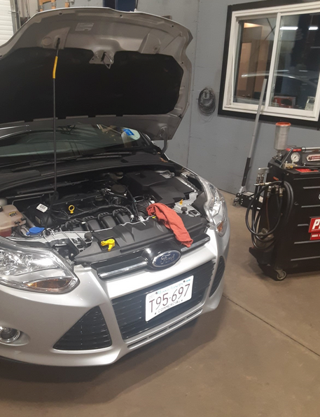 A silver ford car with the hood open in a garage