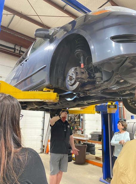 A man is standing under a car on a lift