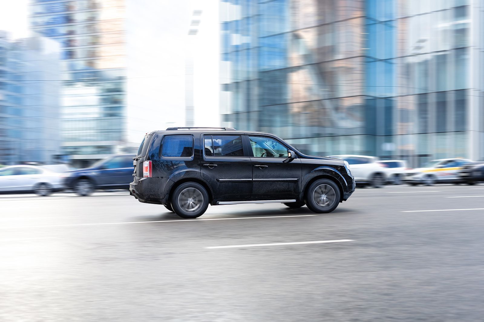 Black SUV driving on a city street, blurred background of buildings and cars.